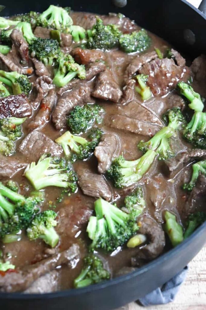 sirloin steak in small pieces with broccoli florets in a brown sauce in a black large skillet