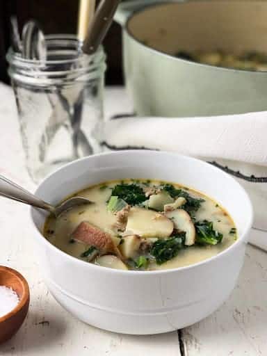 bowl on sausage and kale soup in front of pot and glass cup.