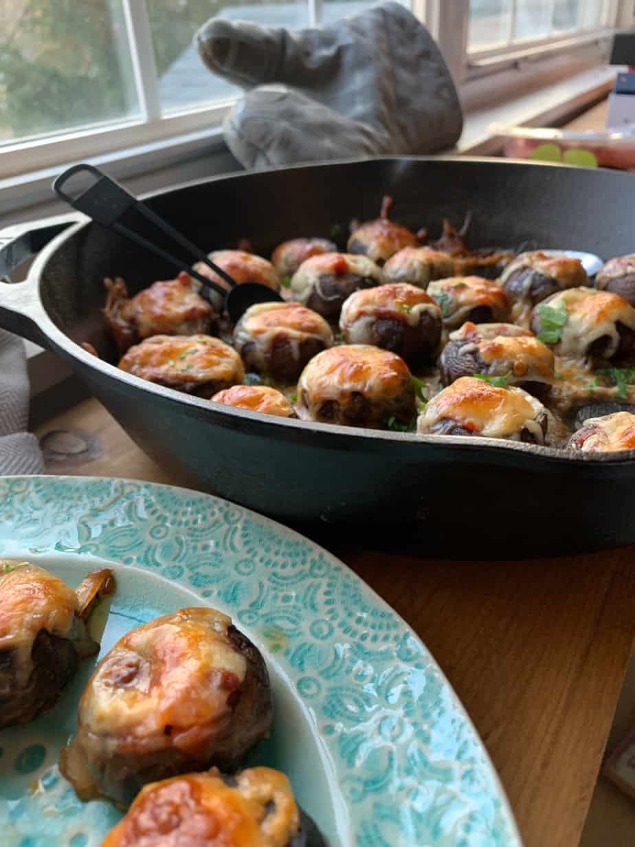 skillet filled with mushrooms in back of plate with a few on it. 