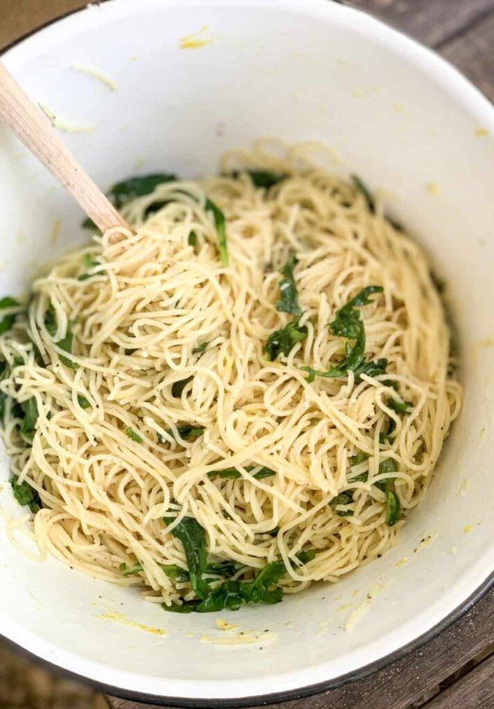 lemon capellini salad in a white bowl being stirred with a wooden spoon.