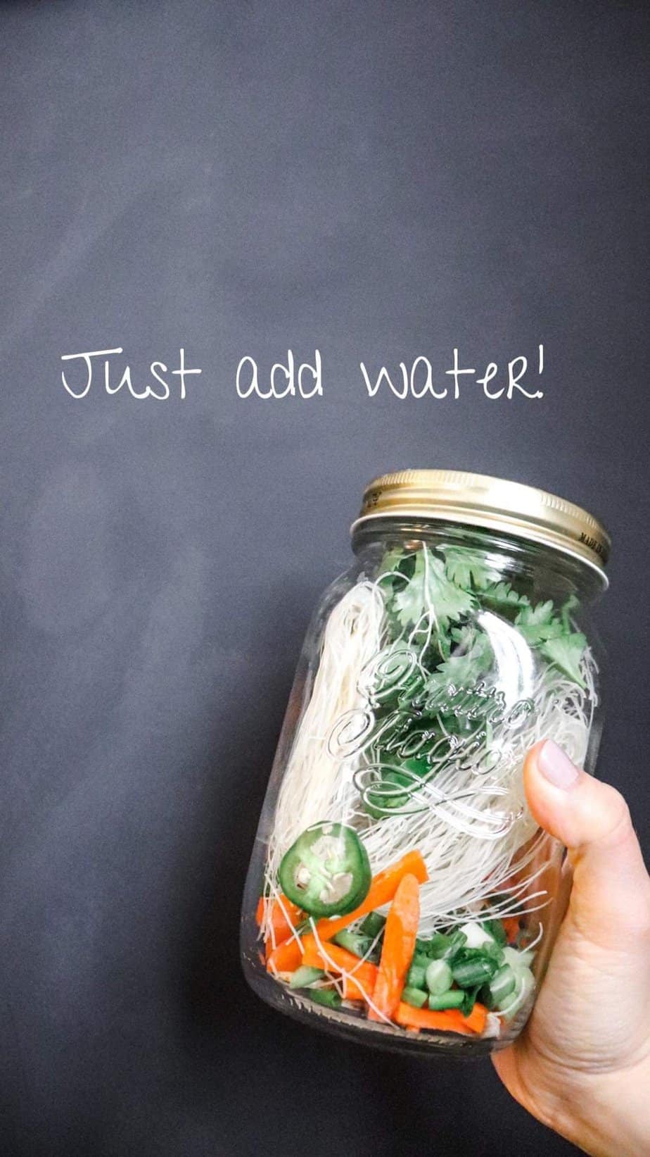 hand holding mason jar noodle cup with words "just add water" written in the background.