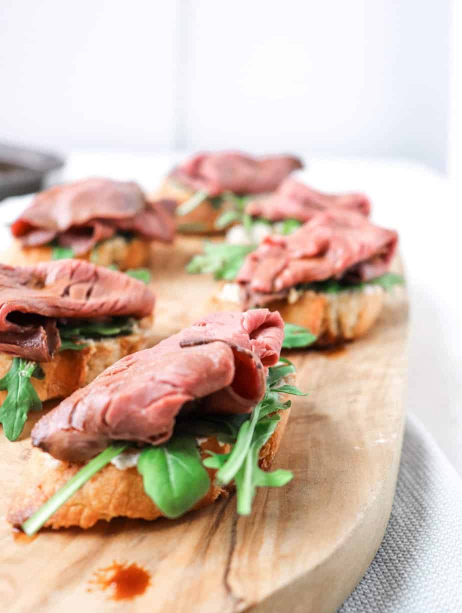 steak, arugula, and toasted bread appetizer on a wooden board