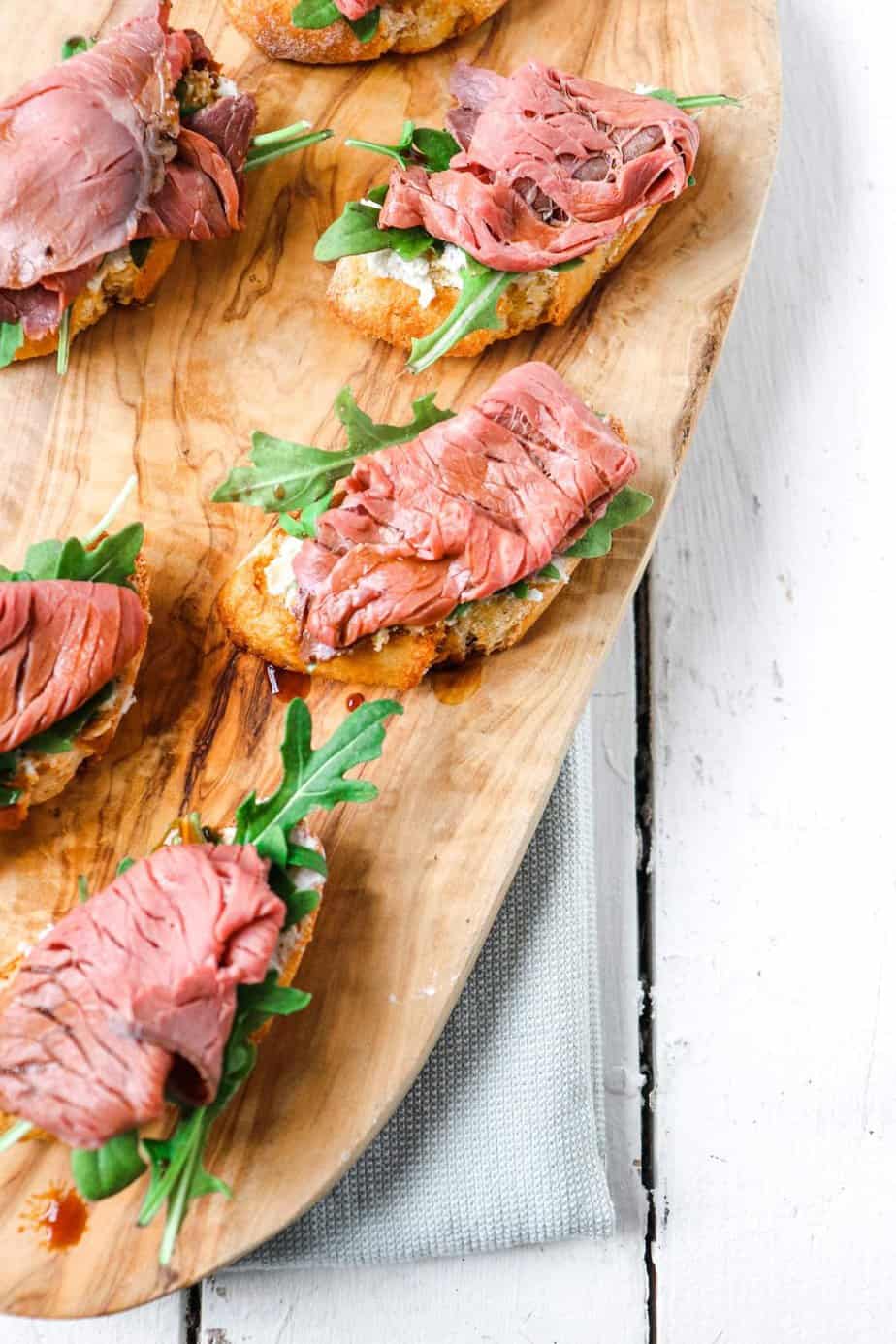 overhead shot of multiple steak and arugula appetizers on a wooden board 