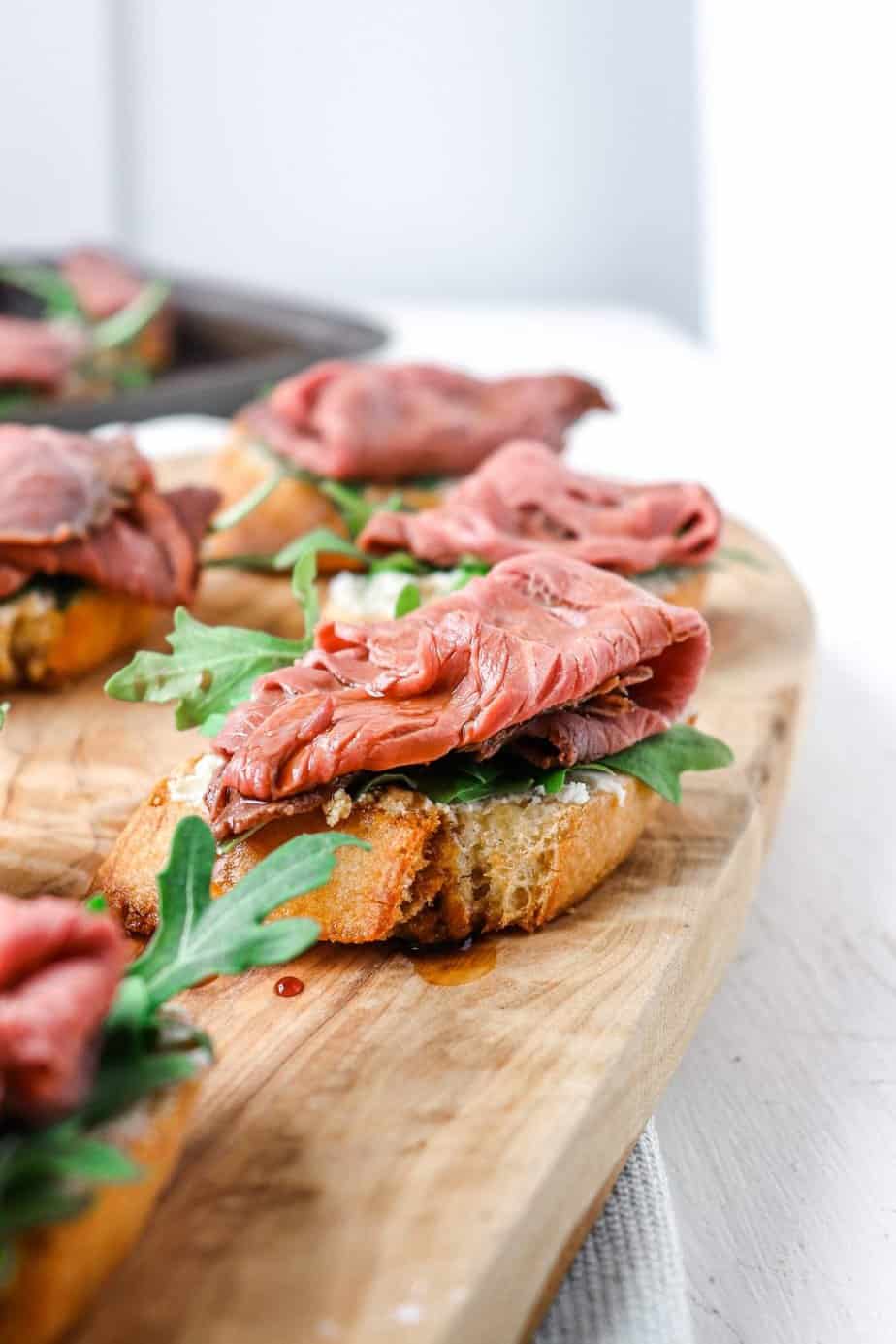 side shot of multiple steak crostini on a wooden board