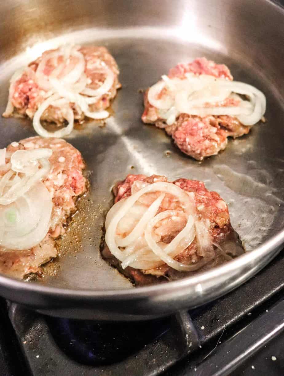 mini burgers with onions in a skillet.