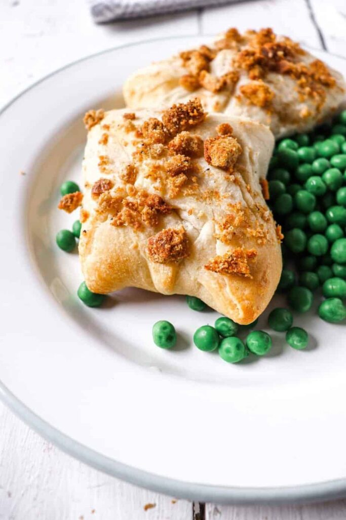 two chicken packets on a white plate with a bed of peas to the side