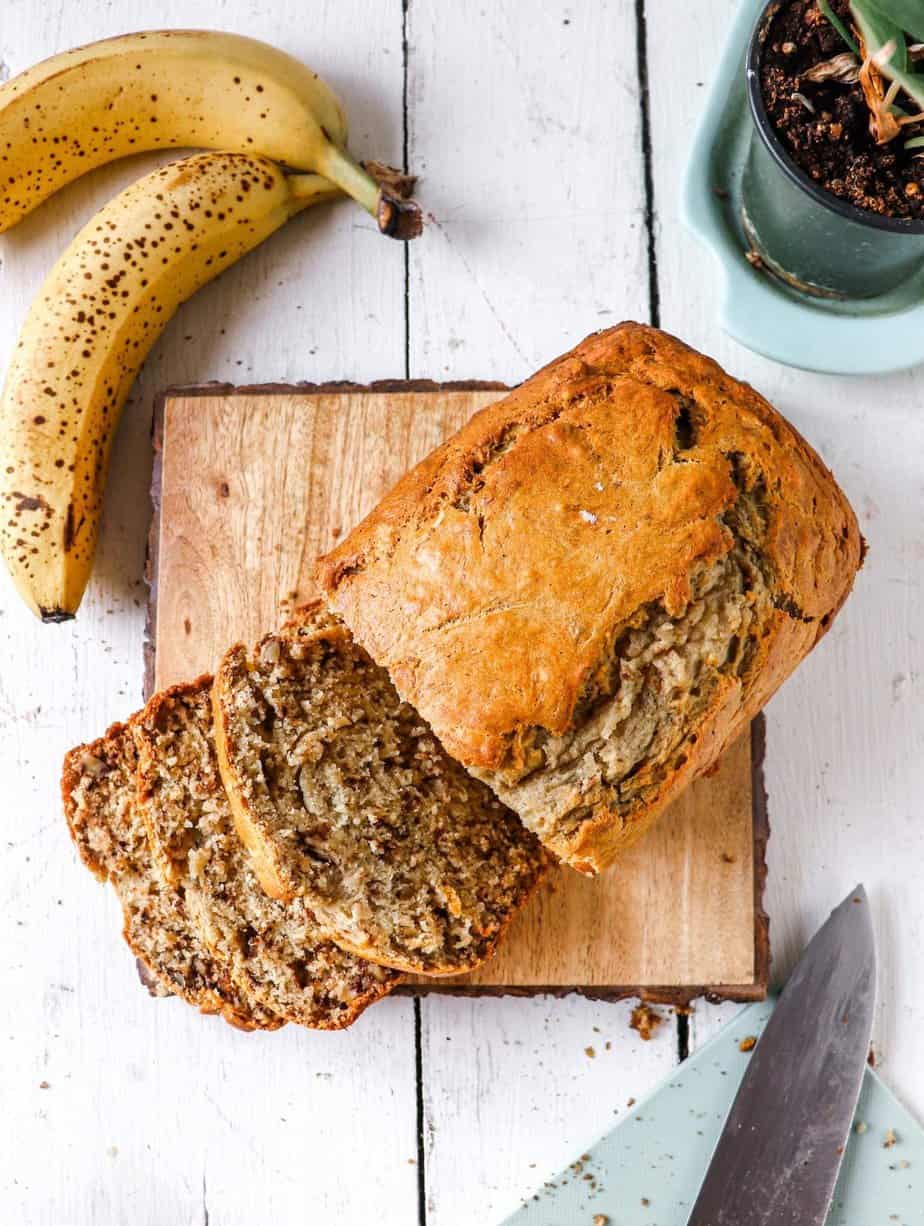 banana bread being sliced with ripe bananas to the side.
