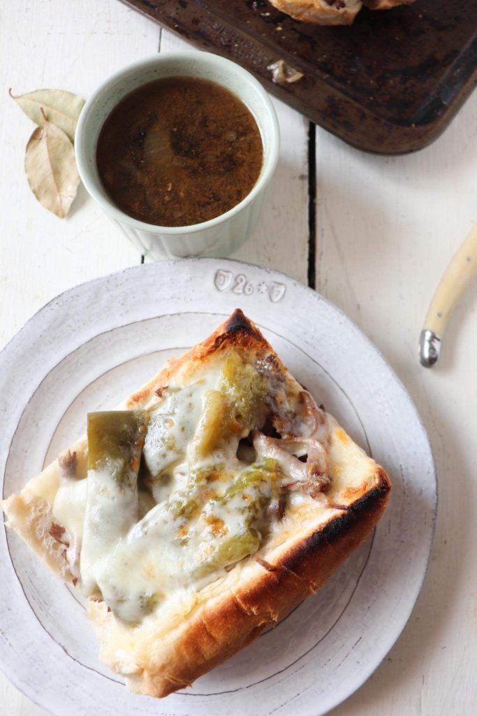 one sandwich on a white plate, open faced with melted cheese on top. A ramekin of juice is next to the plate with a bay leaf