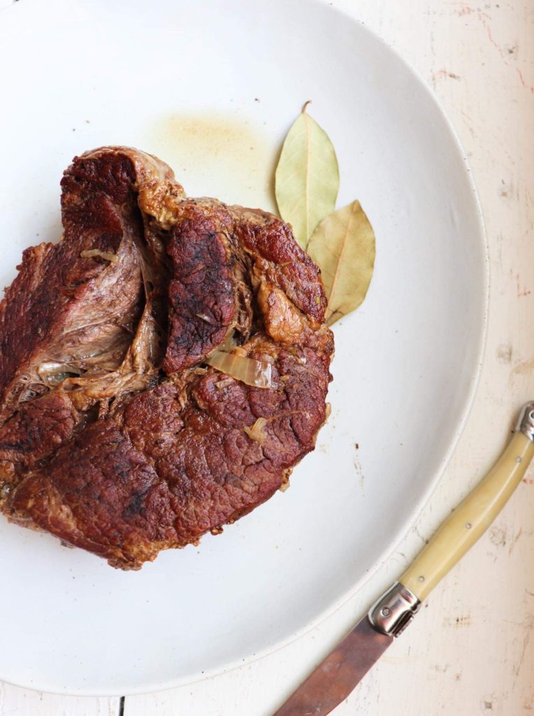 browned chuck roast on a white plate with two bay leaves for garnish