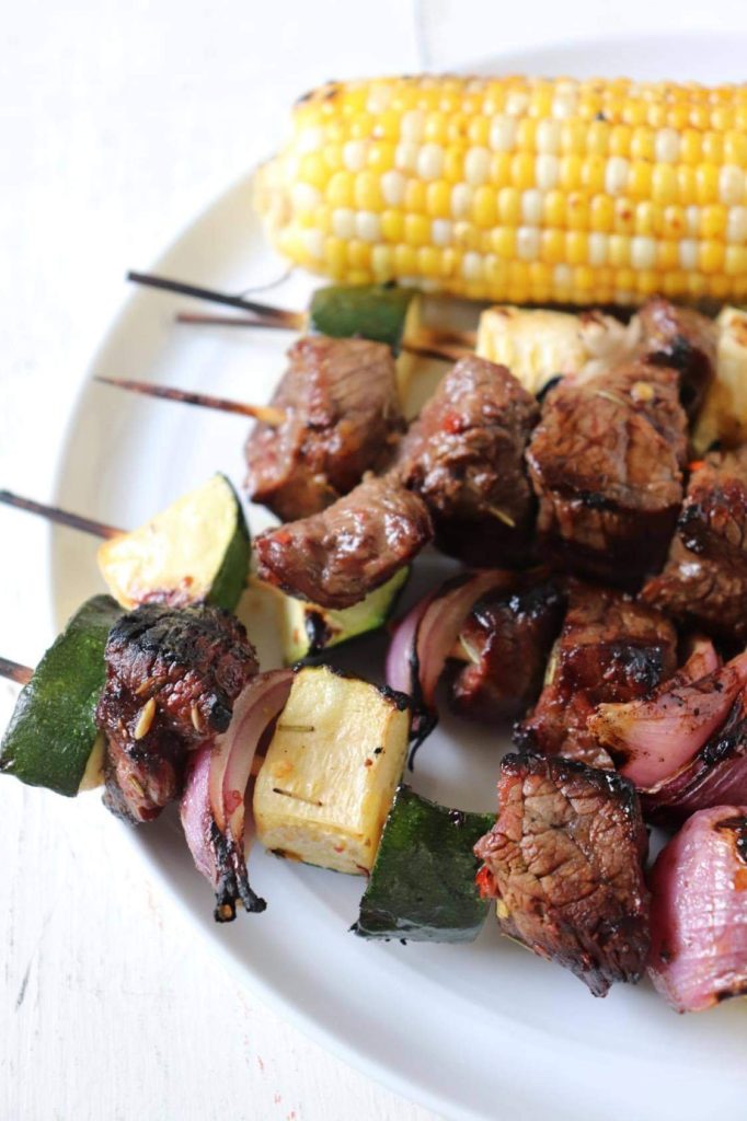 grilled beef and veggie shish kabobs with an ear of corn in the background. 