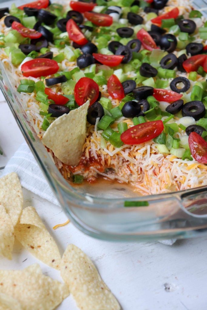 finished pan of taco dip with a chip scooping some.