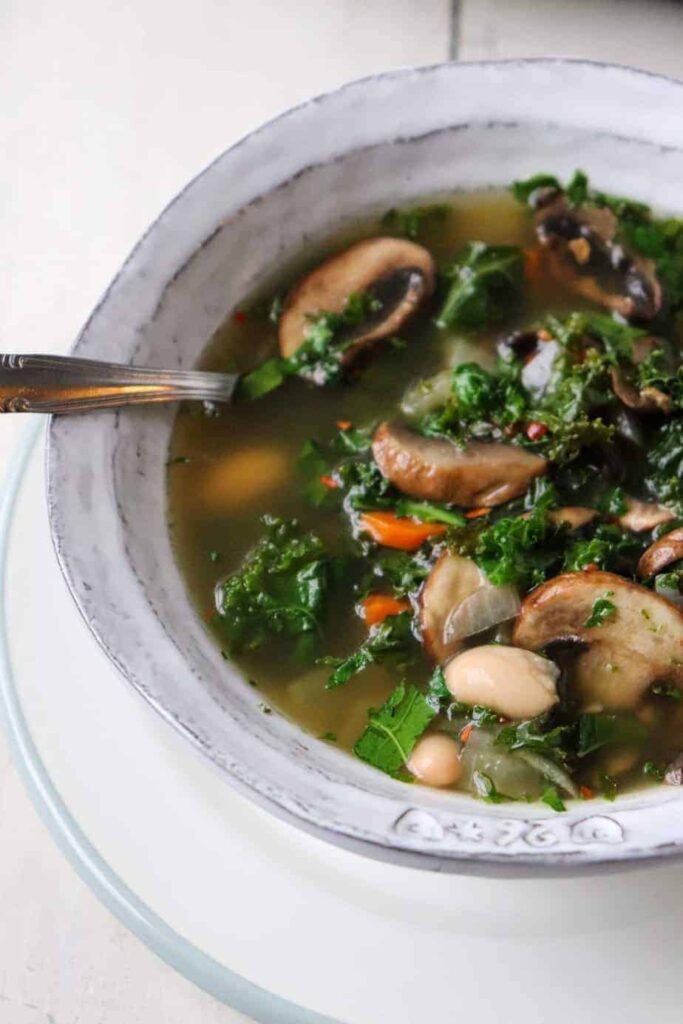 angled overhead shot of mushroom kale soup with a metal spoon coming out of the bowl