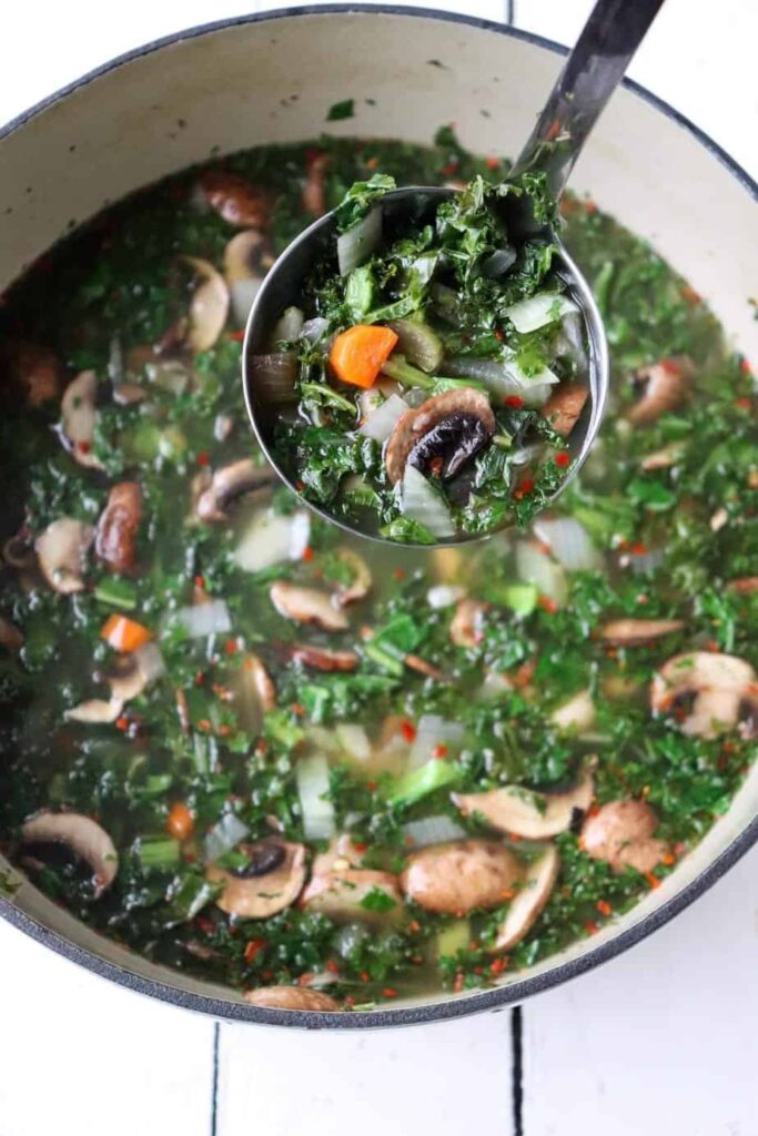 overhead shot of soup in a large part with a metal ladle filled with soup coming towards the camera