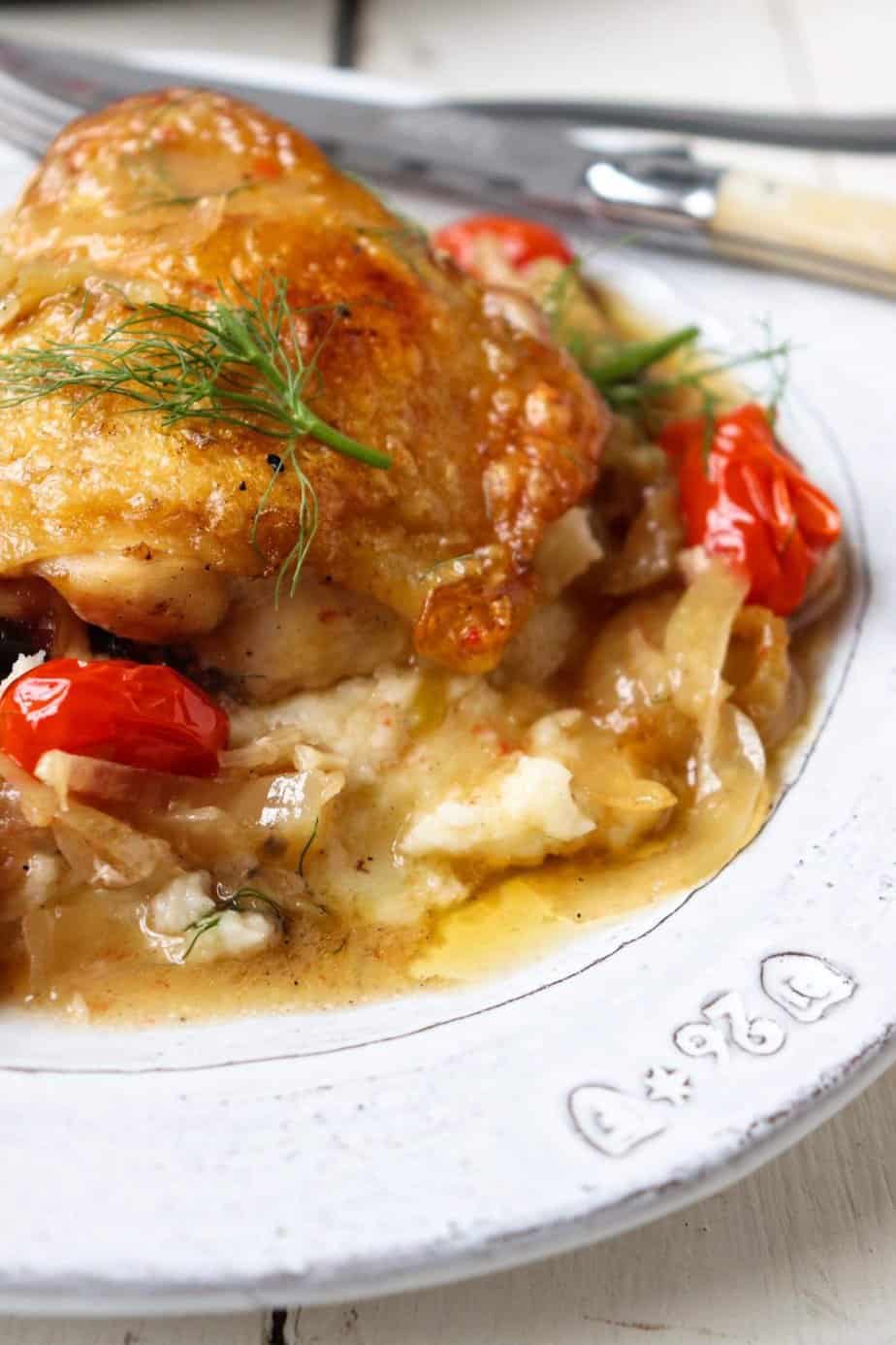 chicken thigh plated on a bed of tomatoes and fennel on a white plate.