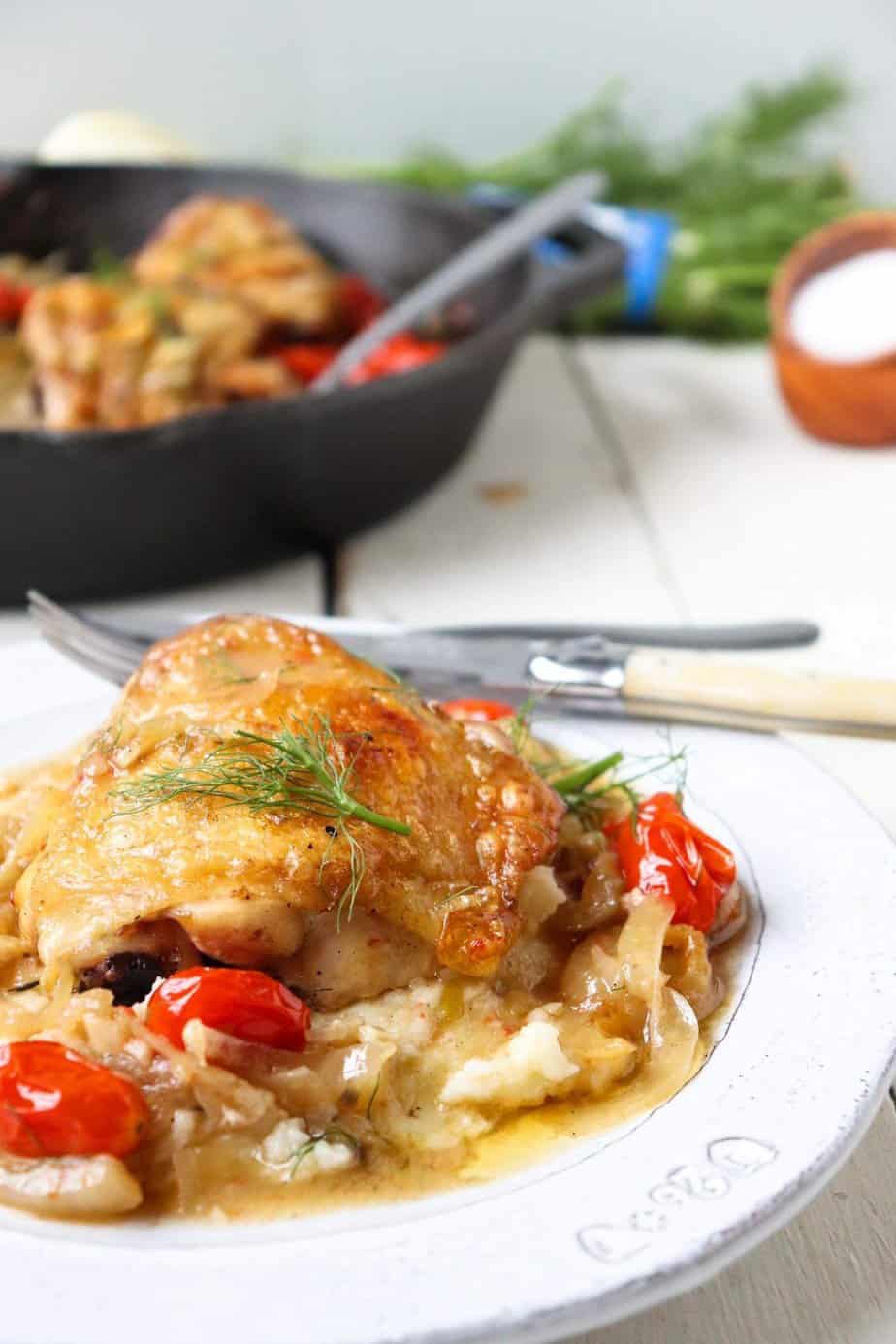 crispy chicken thigh plated on a bed of tomatoes and fennel topped with fresh herbs.