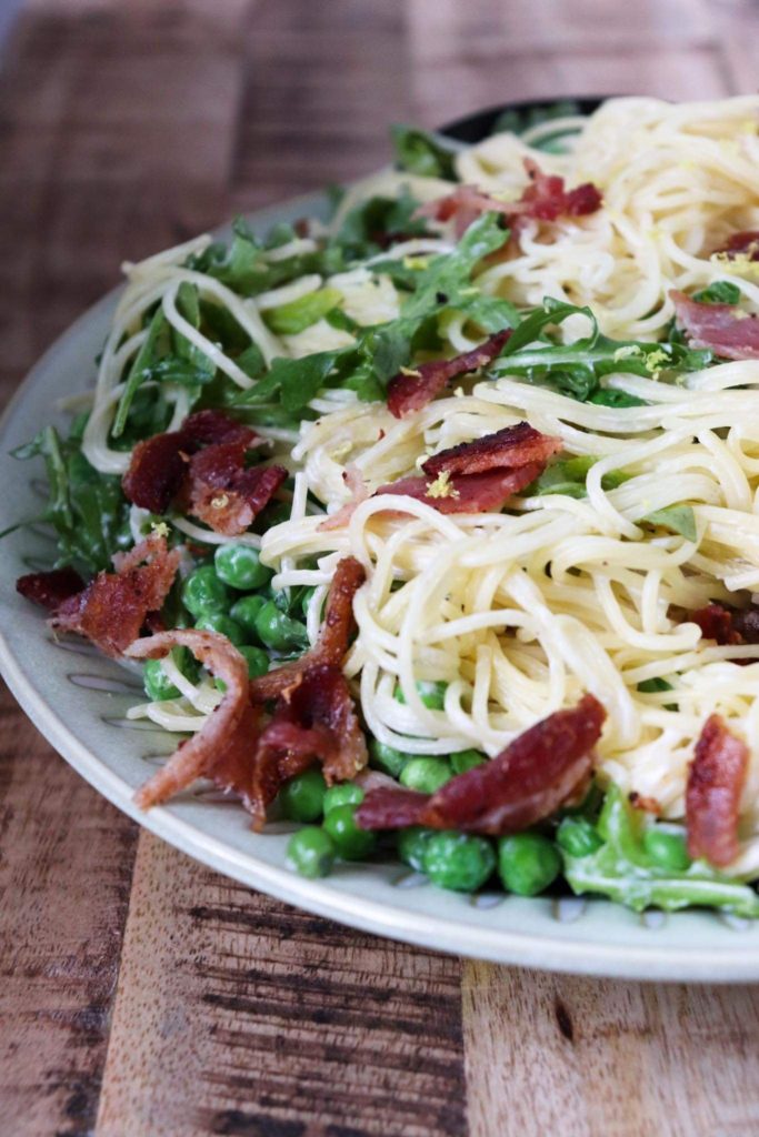 finished pasta with peas and bacon on a decorative plate.