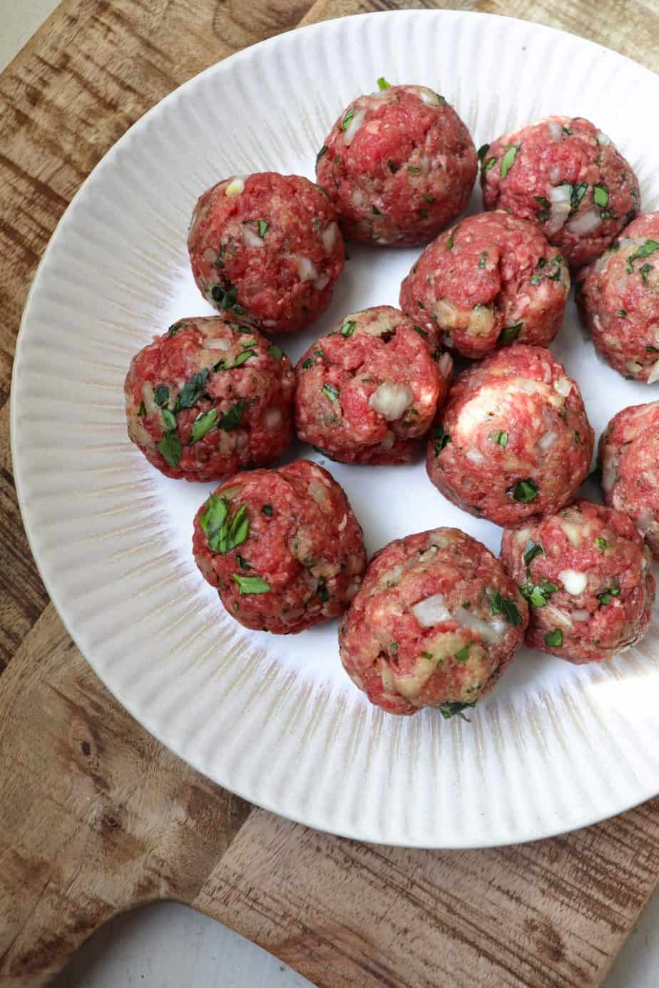 rolled meatballs that are uncooked on a plate.