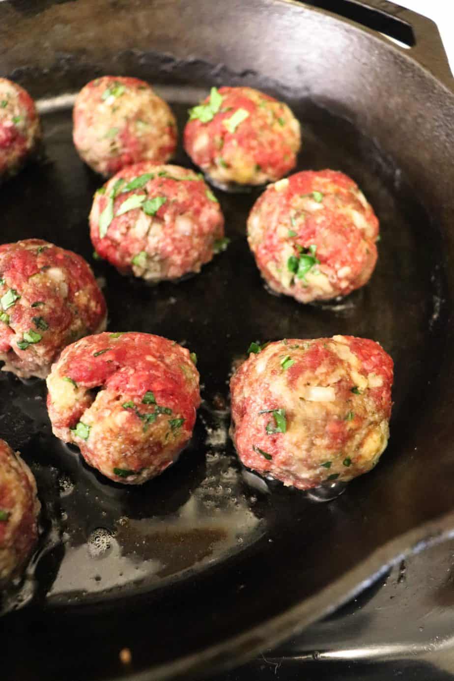 meatballs cooking in a cast iron skillet.