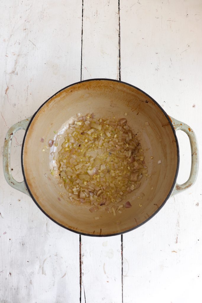 shallots and garlic sauteed in a large pot on a white background