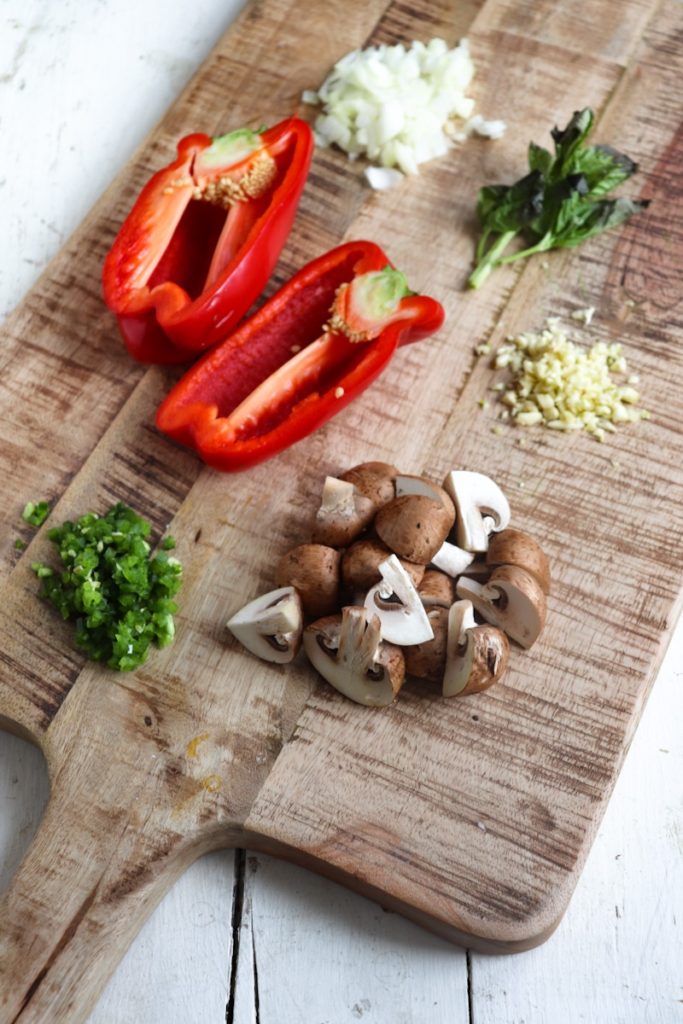 red bell pepper, diced yellow onion, chopped cremini mushrooms, minced jalapeno, minced garlic, and basil on a wooden cutting board