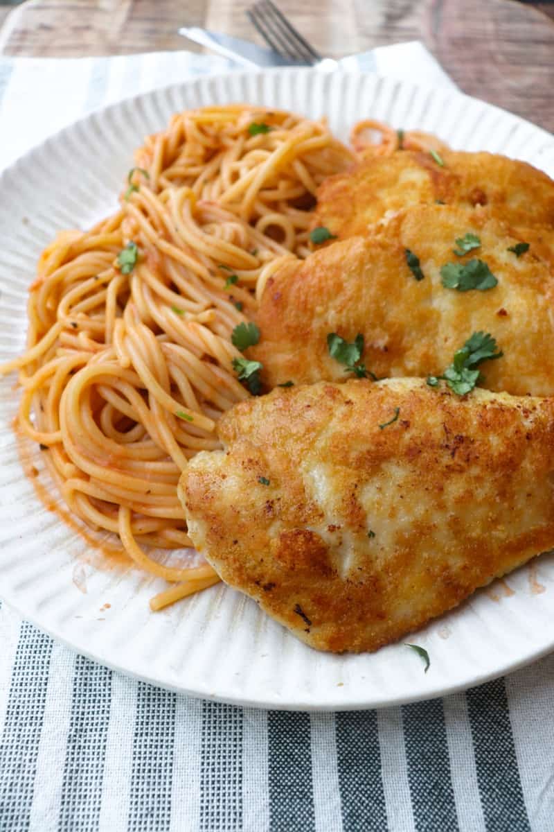 chicken on a white plate with spaghetti  and a green and white striped napkin