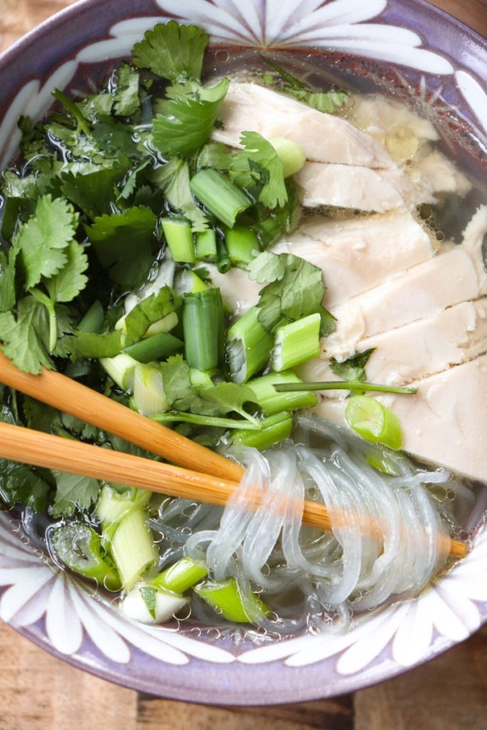 chicken soup with herbs on top with chopsticks resting on a purple bowl