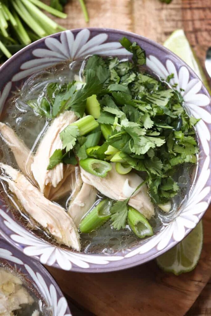 mien ga soup in a purple bowl topped with fresh herbs and shredded chicken pieces