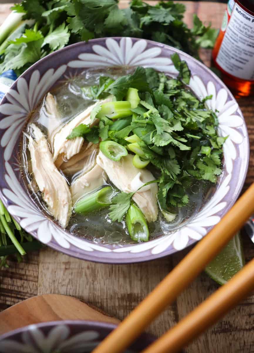 mien ga with herbs and chicken in a purple bowl on a wooden background with additional ingredients scattered around