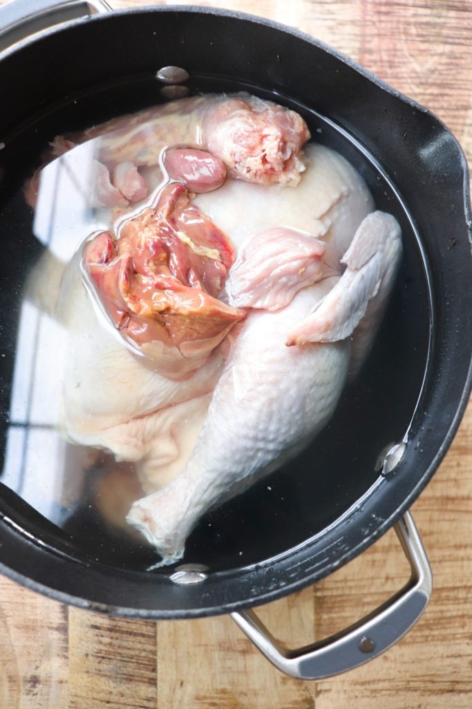 whole chicken covered in water with the gizzards on top in a big pot