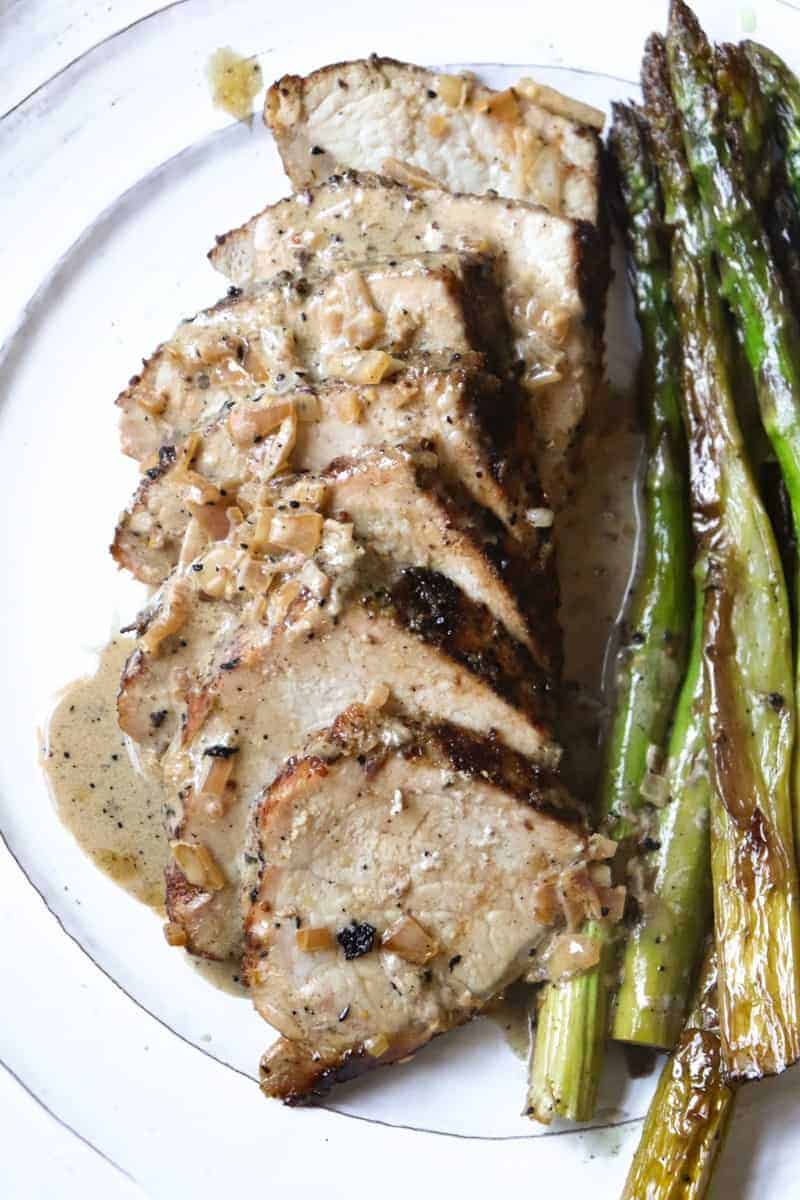 pork tenderloin slices topped with cream sauce plated  next to asparagus.