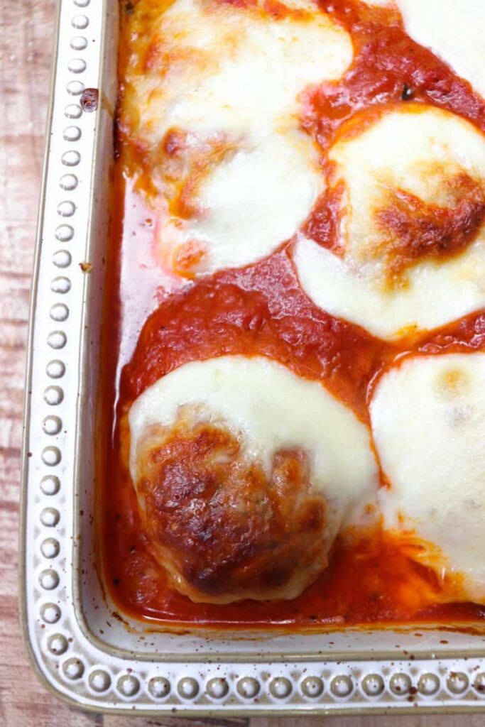 Chicken parmesan cooked in a cream colored baking dish. Covered in red sauce and melted cheese.