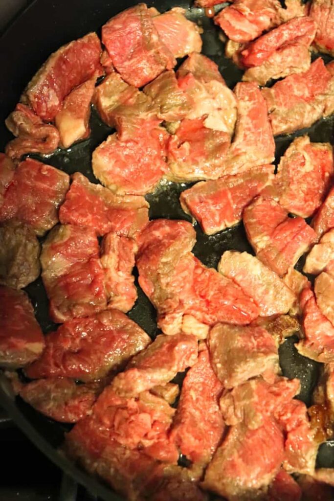 sirloin steak pieces in black large skillet being cooked