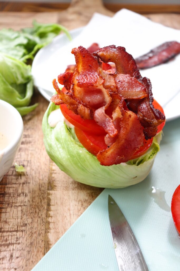 open-faced lettuce half with ranch, tomato, and bacon piled on top. Prep ingredients in background