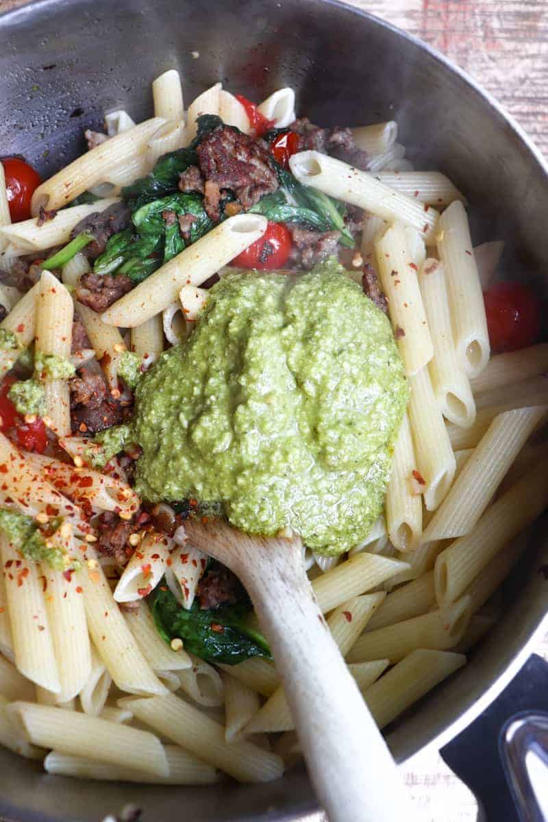 pasta and pesto added to ingredients in the pot.