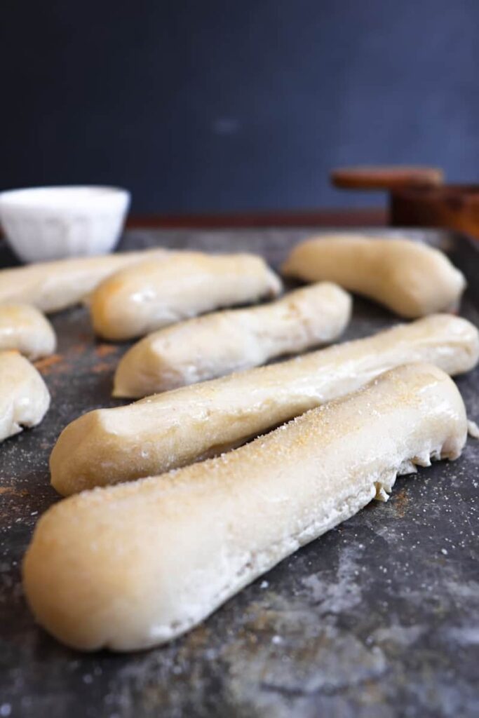 close up of finished breadsticks with a small white bowl and wooden salt container in background
