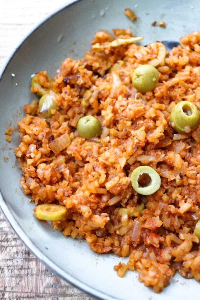 overhead shot of red spanish rice with sliced green olives on top in a shallow grey bowl