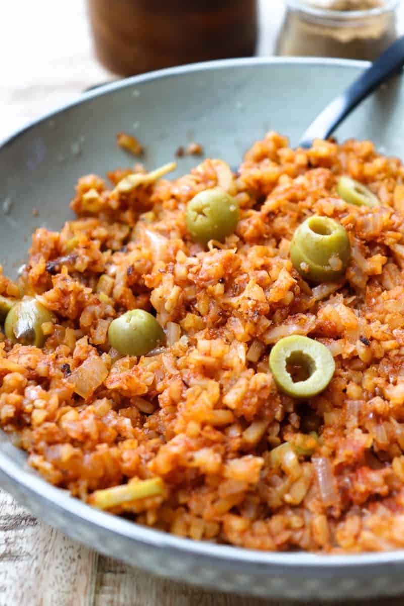 angled shot of red spanish rice with sliced green olives on top in a shallow grey bowl