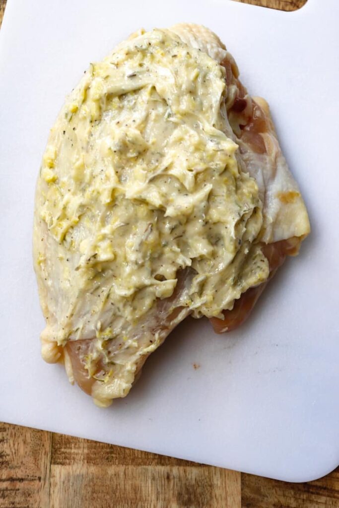 raw chicken on a white plastic cutting board covered in herb-garlic butter