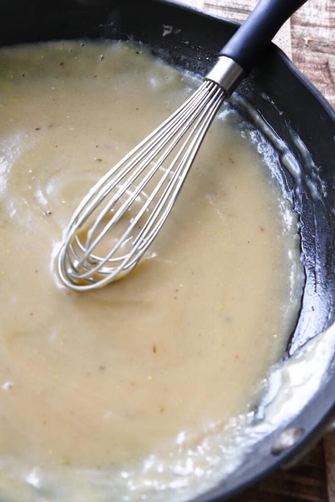 completed gravy in a dark grey skillet with a whisk at an angle