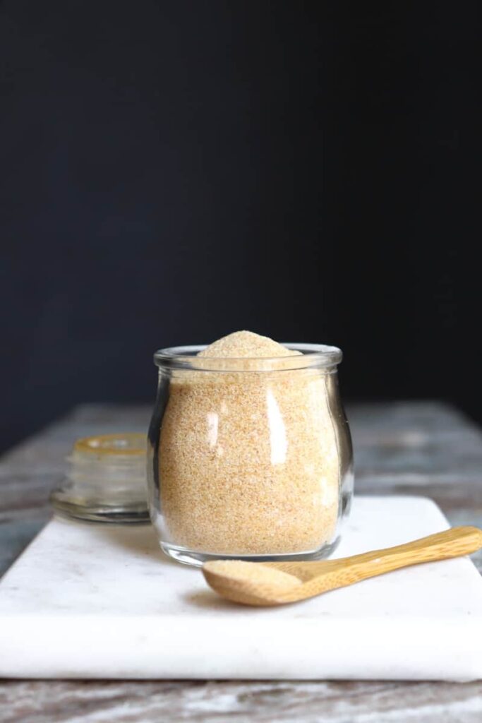 garlic powder in a glass jar with a wooden spoon placed at an angle in front on a white marble cutting board