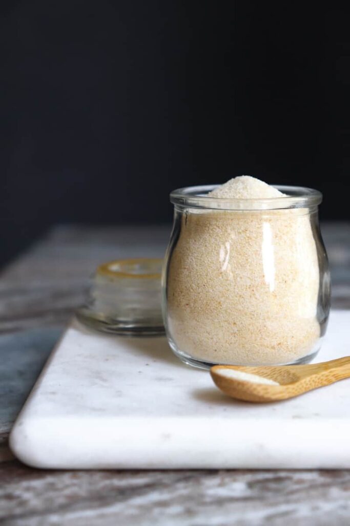 onion powder in a glass jar with a wooden spoon placed at an angle in front on a white marble cutting board