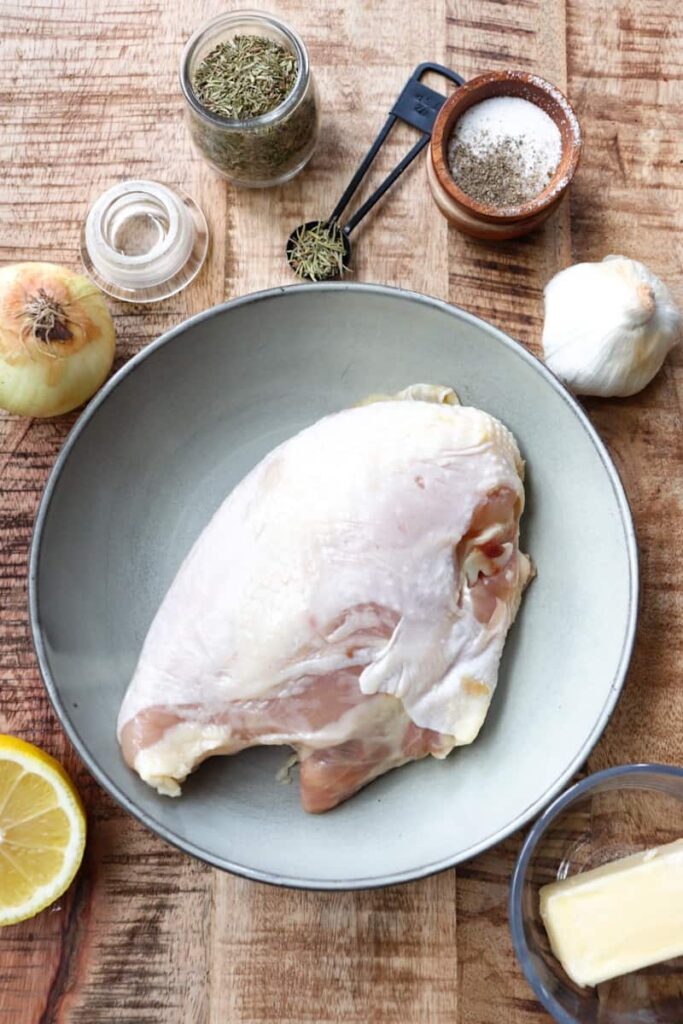 raw chicken on a grey plate with other ingredients scattered around it on a wooden background