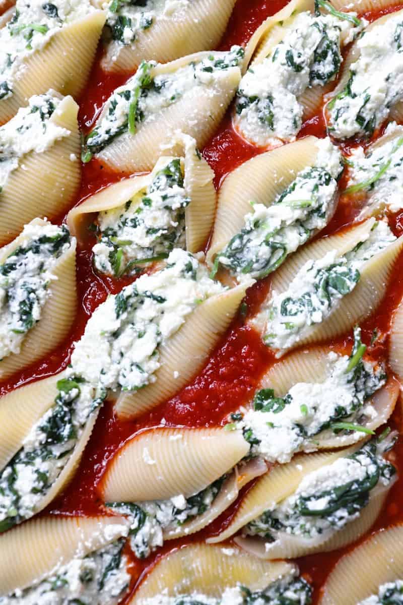 multiple uncooked shells stuffed with cheese and spinach filling in red sauce
