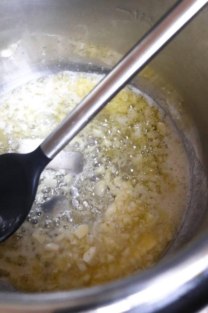 garlic sauteing in butter and olive oil with spoon coming out of the instant pot at an angle