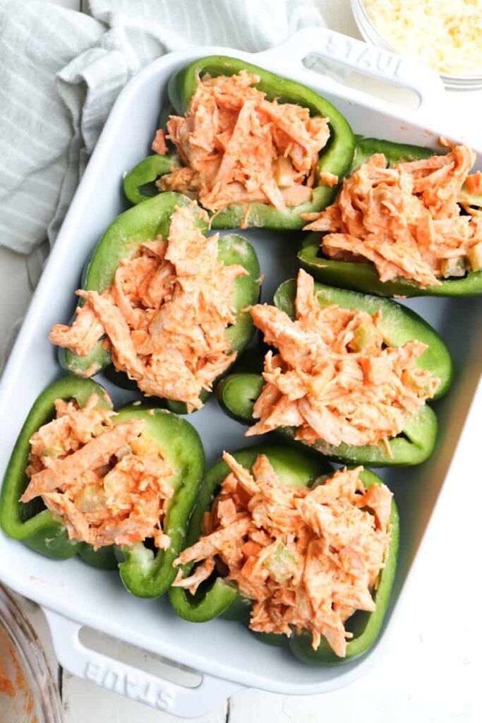 green peppers stuffed with shredded chicken mixture in a baking dish