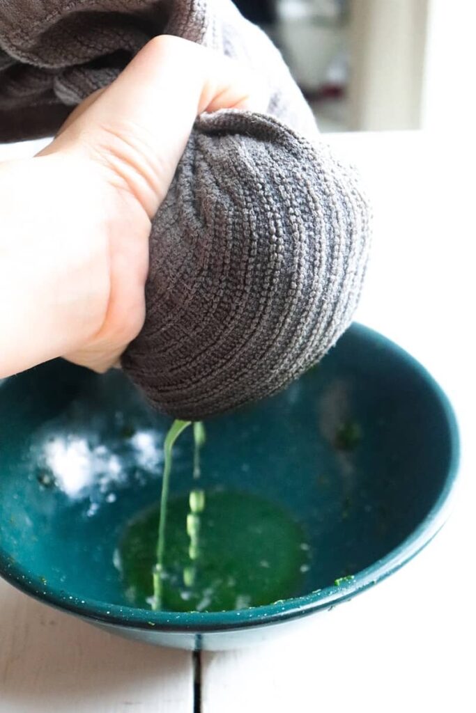water being squeezed out of frozen spinach covered in a towel into a green bowl