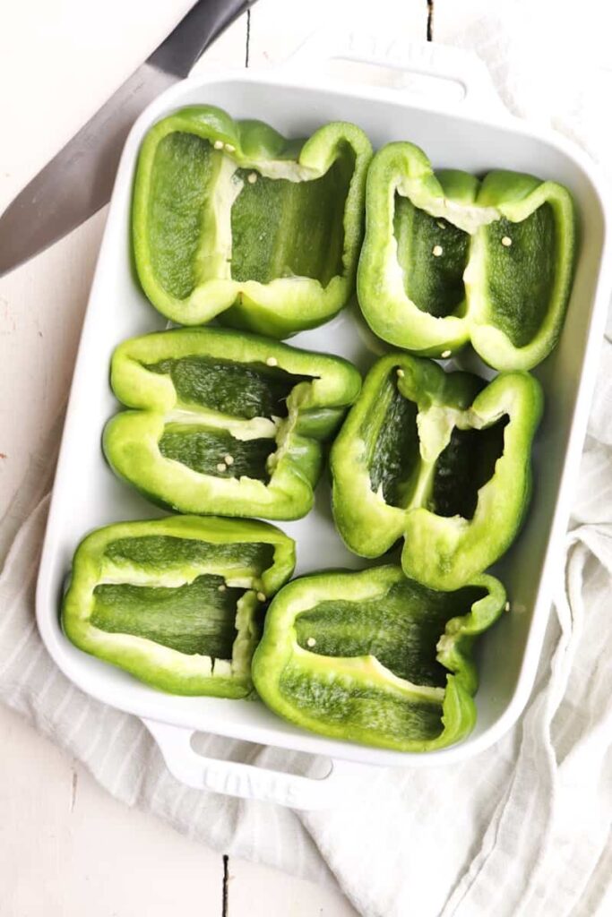 sliced green bell peppers cut side up in a white baking dish