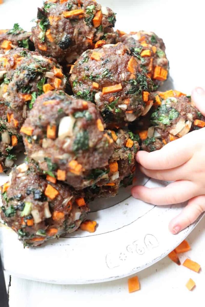 finished sweet potato meatballs with a babies hand grabbing one