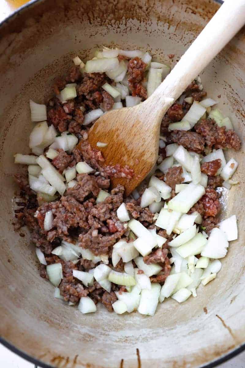 italian sausage with diced onions and garlic that have just been stirred in with a wooden spoon
