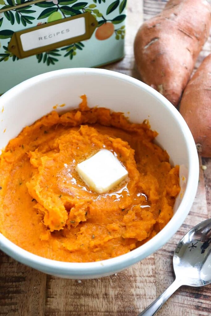 sweet potatoes with a pad of butter on top with recipe tin and two sweet potatoes in the background
